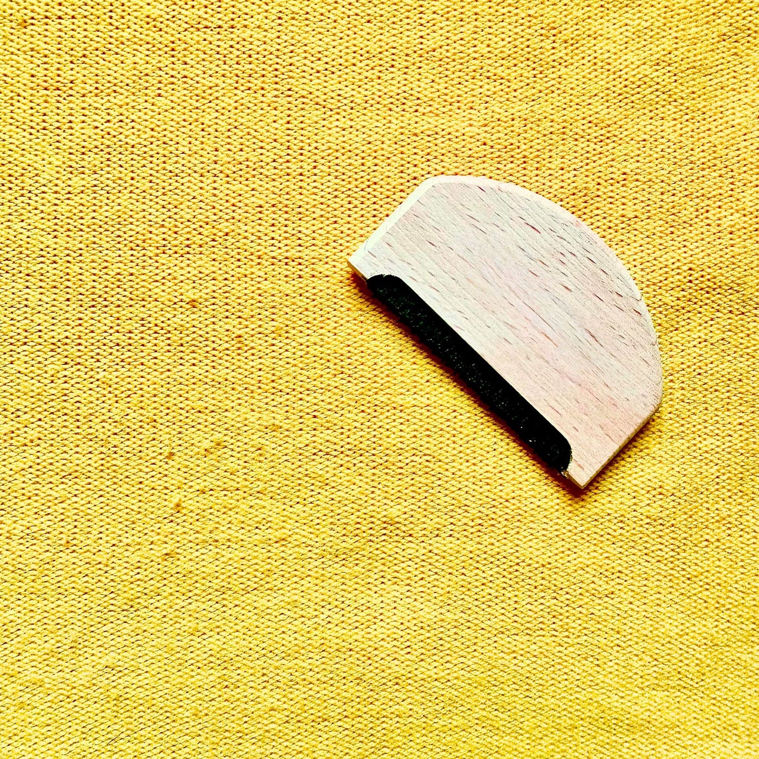 a piece of yellow knitted fabric with bobbles on the surface. a wool comb in birch wood is lying on the fabric.