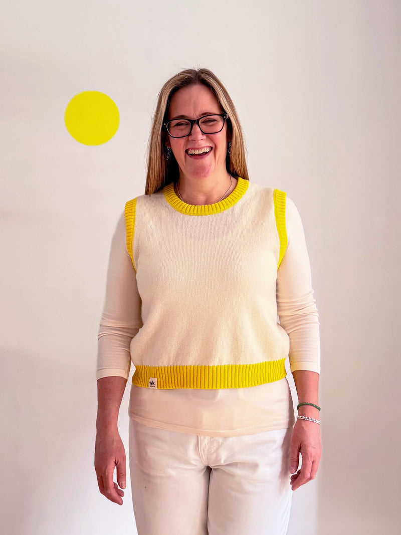 Woman wearing a cream sweater with yellow accents against a plain background