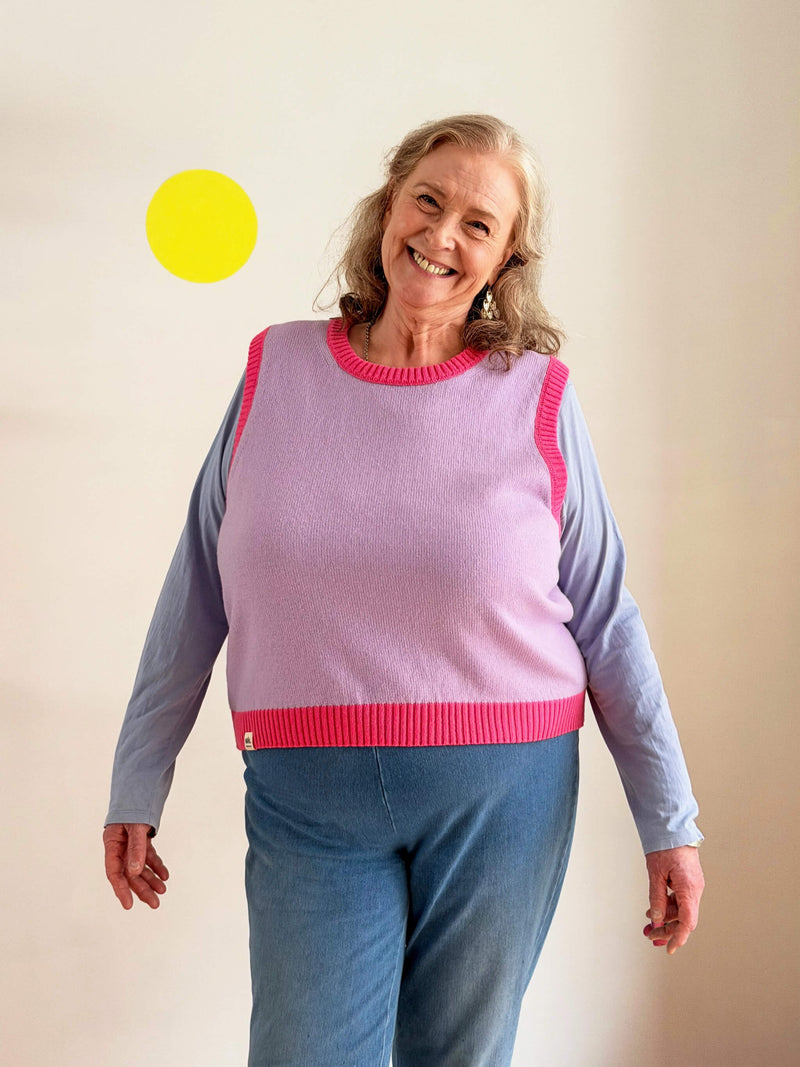 Woman wearing a pink and lilac knitted sweater vest with blue sleeves against a plain background