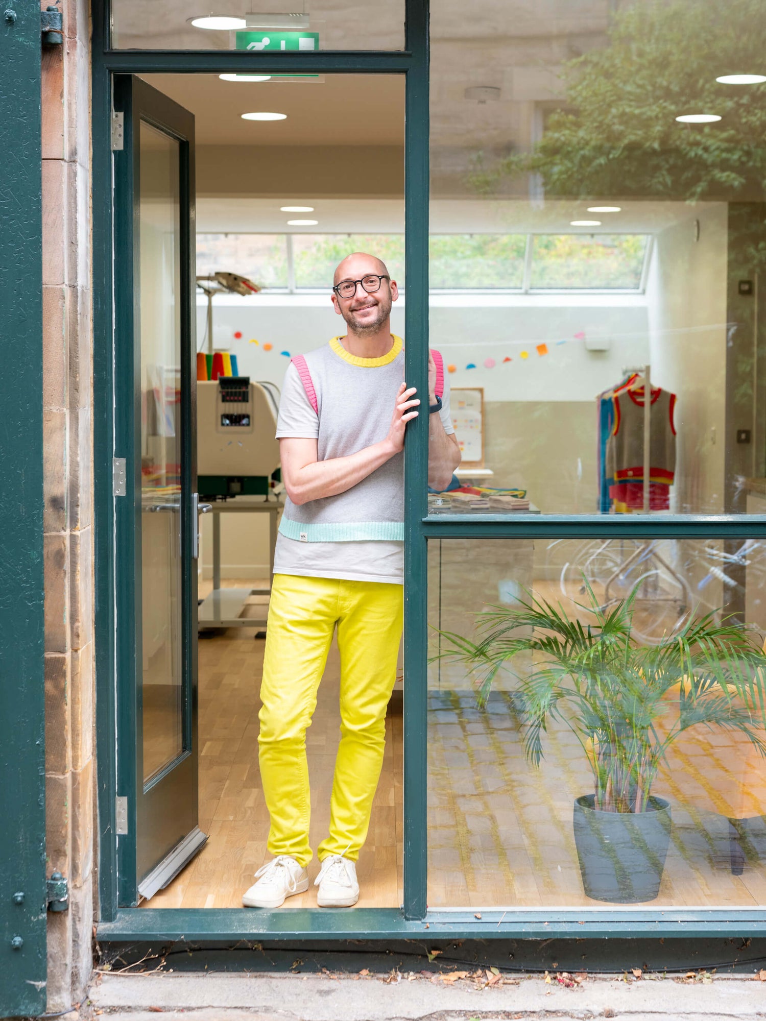 Laurence from Woolkind standing in Marchmont studio doorway with a bright yellow outfit, smiling.