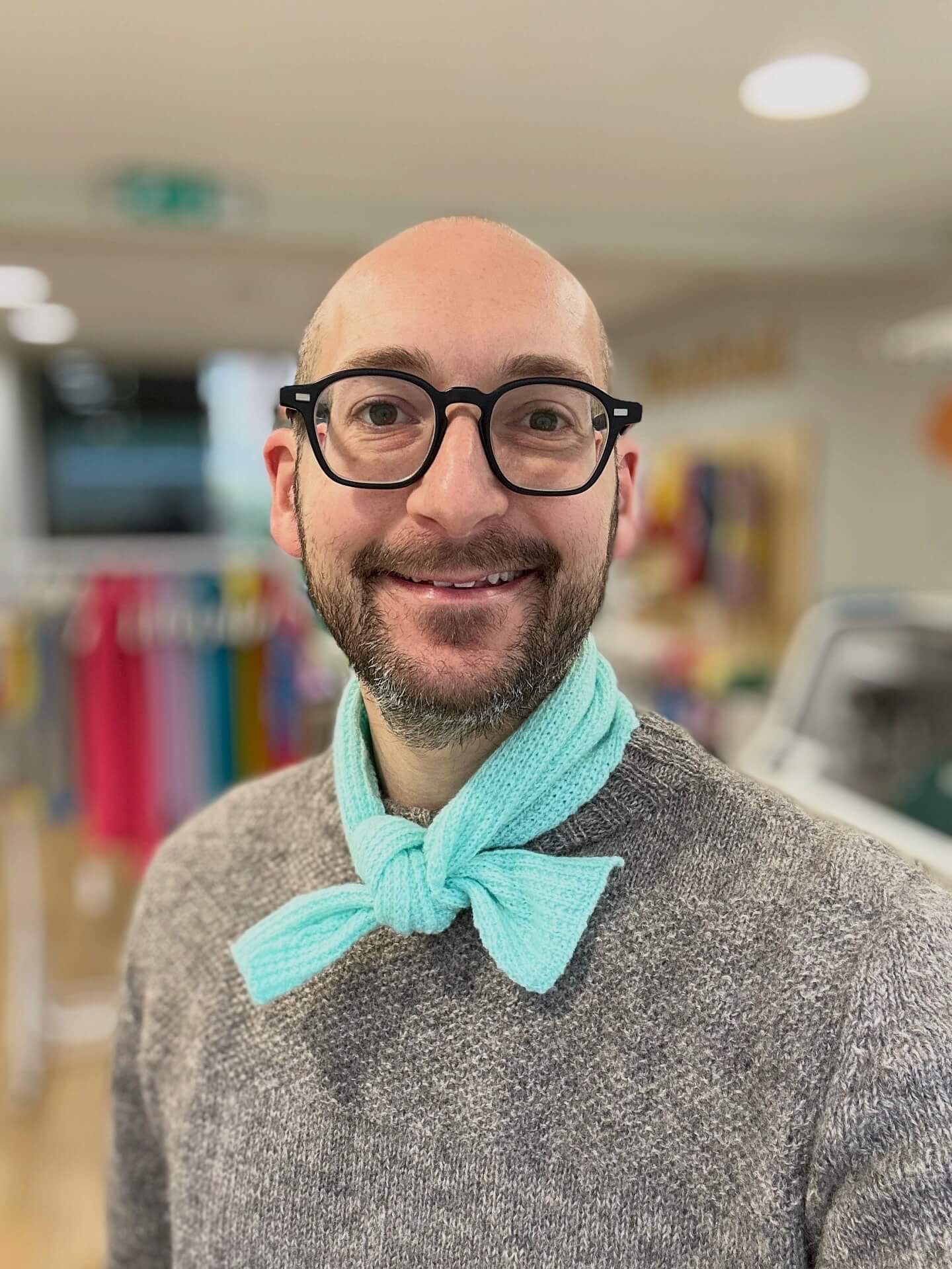Man wearing glasses and a gray sweater with a aqua merino wool neckerchief scarf in an indoor setting - Woolkind