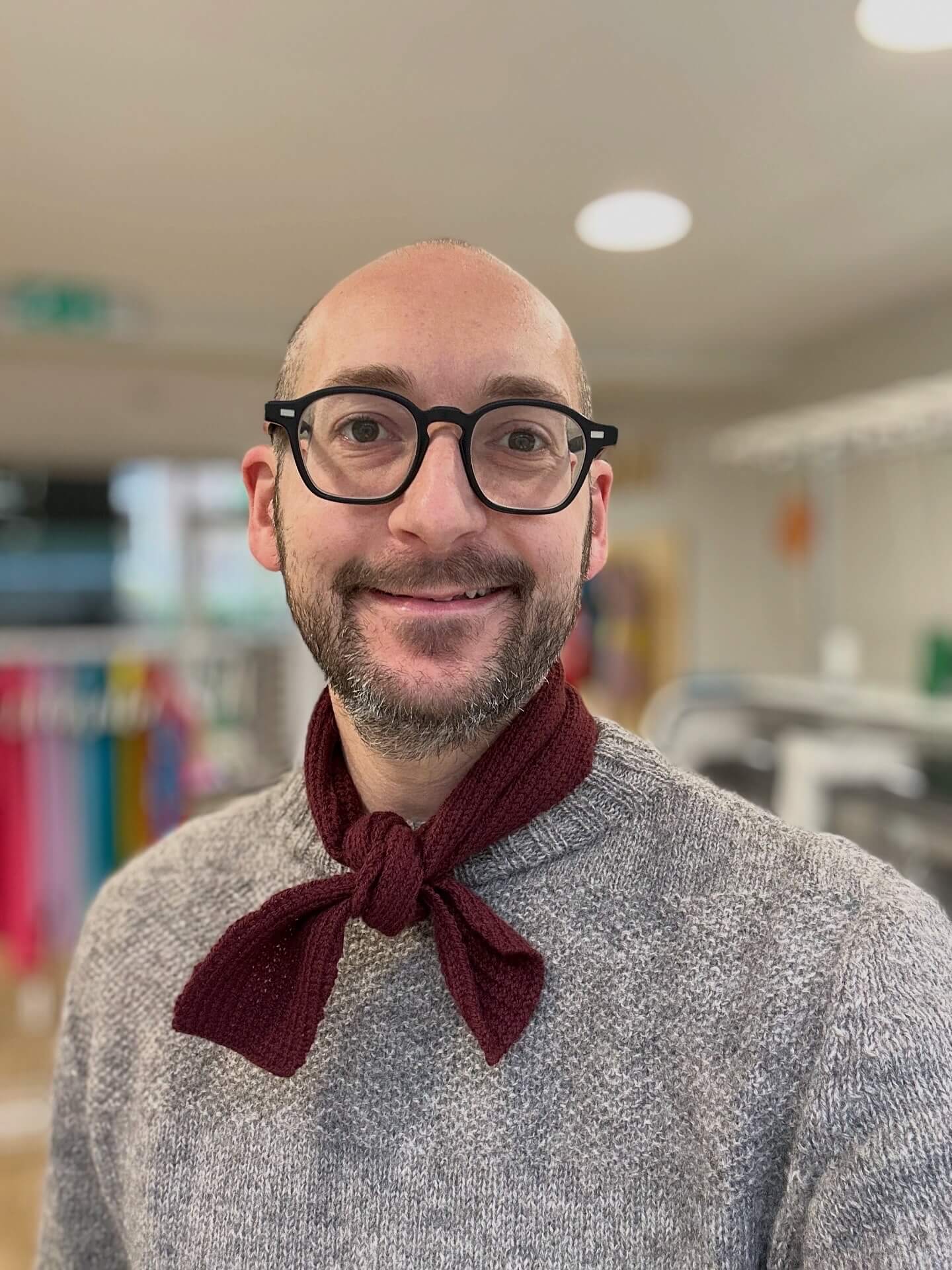Man wearing glasses and a gray sweater with a burgundy merino wool neckerchief scarf in an indoor setting - Woolkind