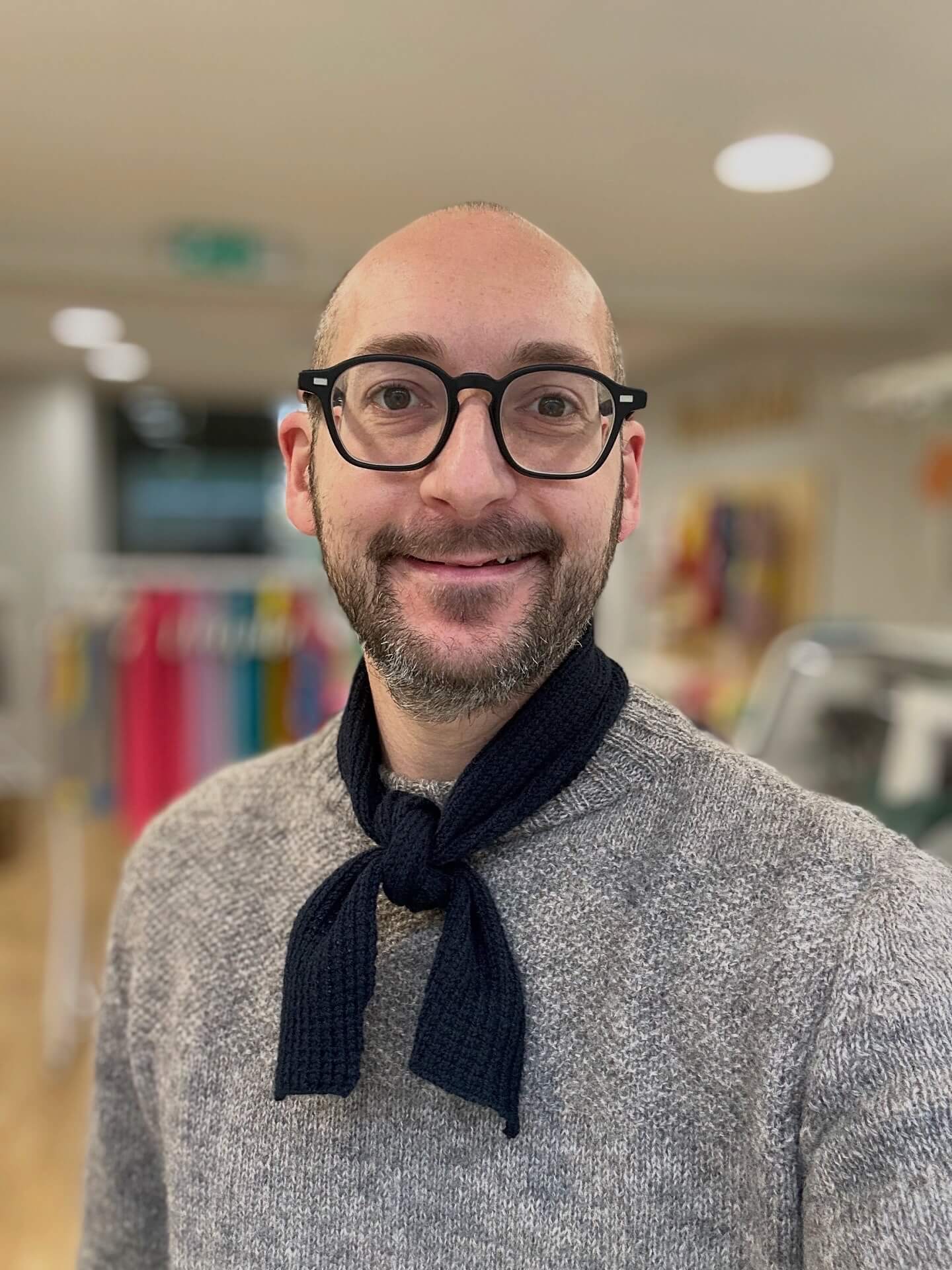 Man wearing glasses and a gray sweater with a navy merino wool neckerchief scarf in an indoor setting - Woolkind