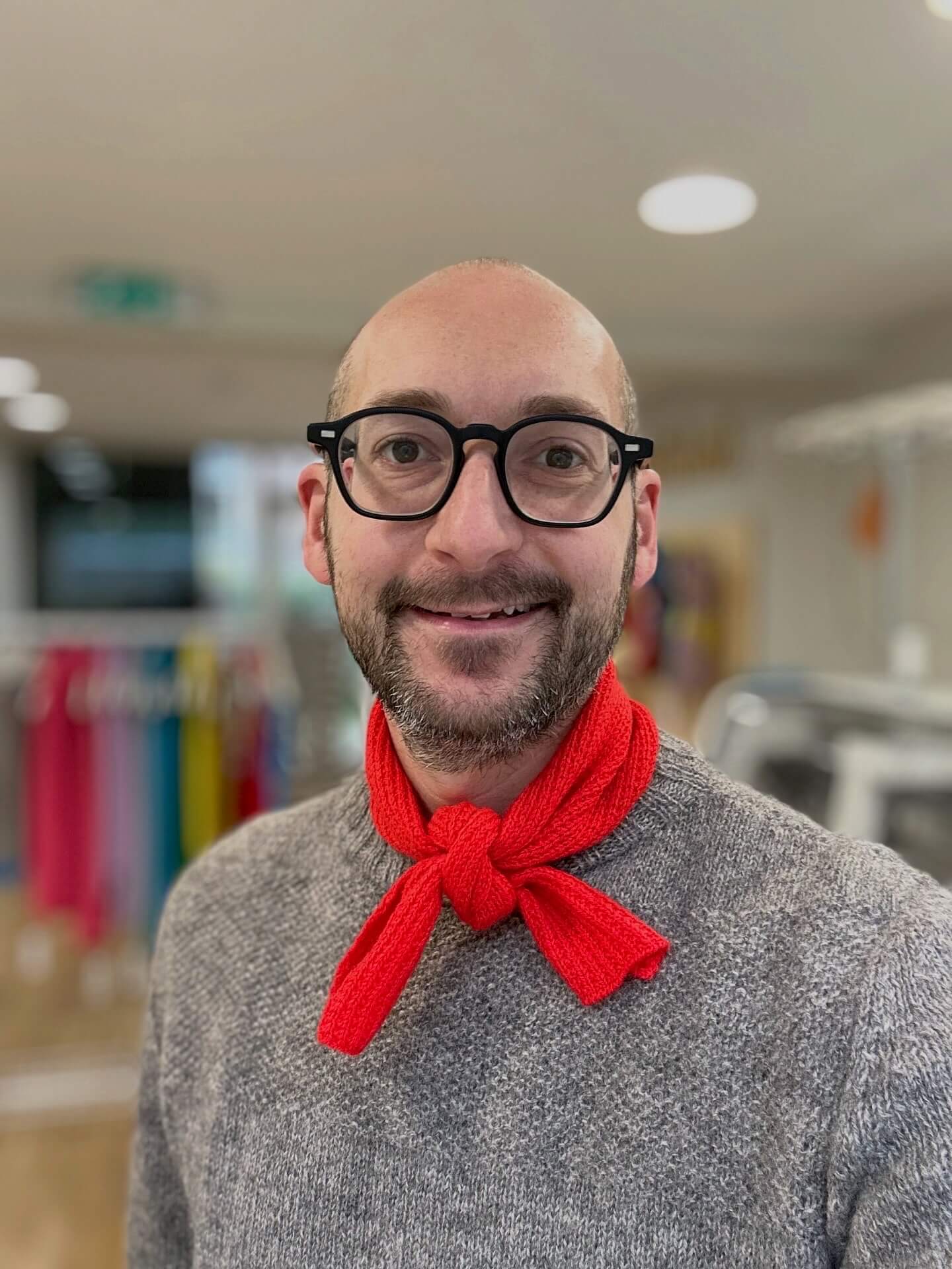Man wearing glasses and a gray sweater with a red merino wool neckerchief scarf in an indoor setting - Woolkind