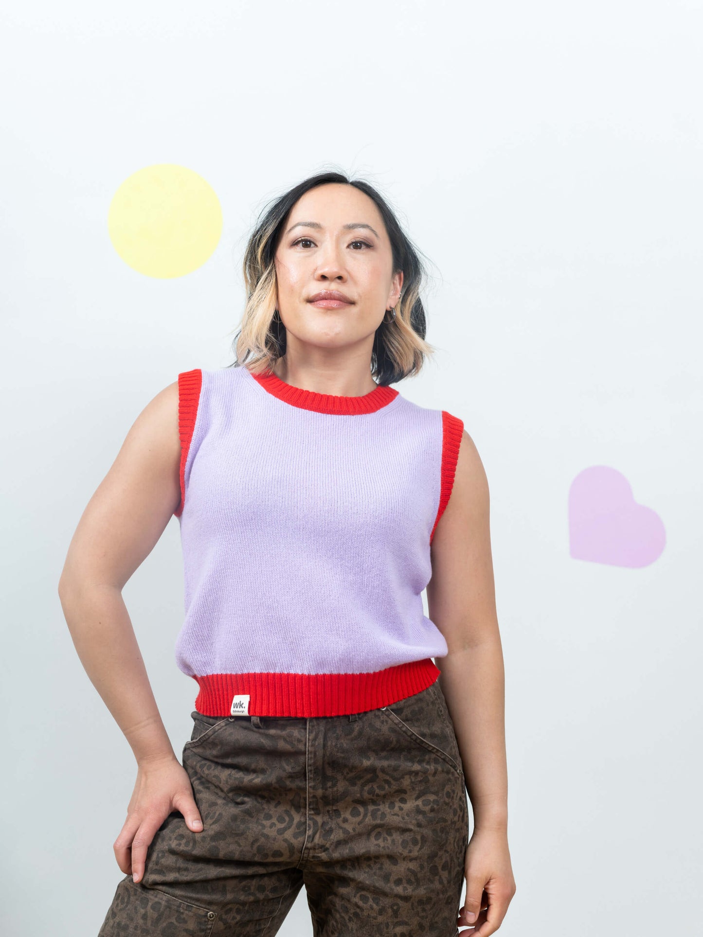 Person wearing a sleeveless purple knitted tank top with red trim against a plain background
